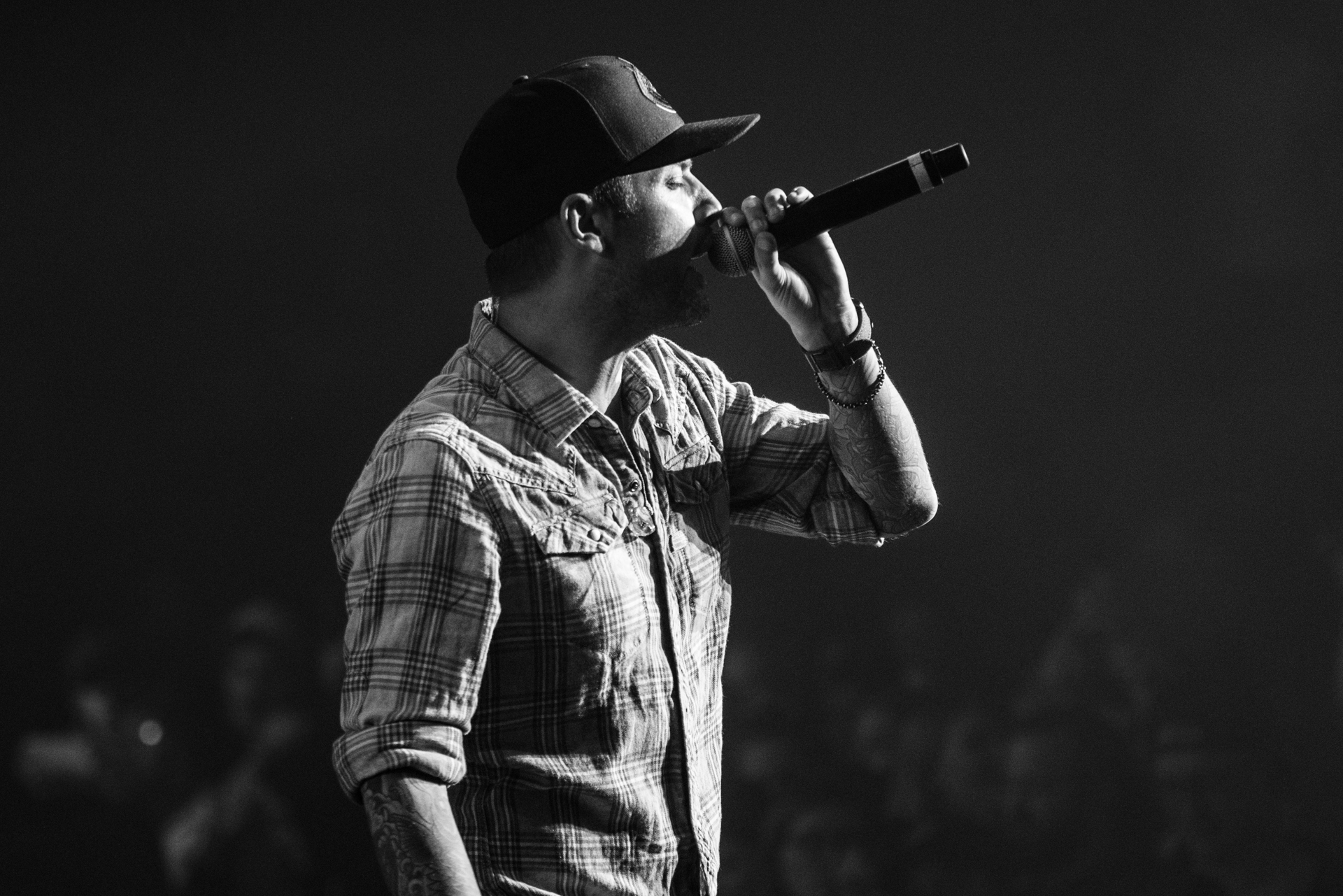 In a captivating black and white photo, Dallas Smith is captured in a side profile, pouring his soul into the microphone. The audience in the background adds depth to the image, illustrating the connection between the artist and the engaged crowd.