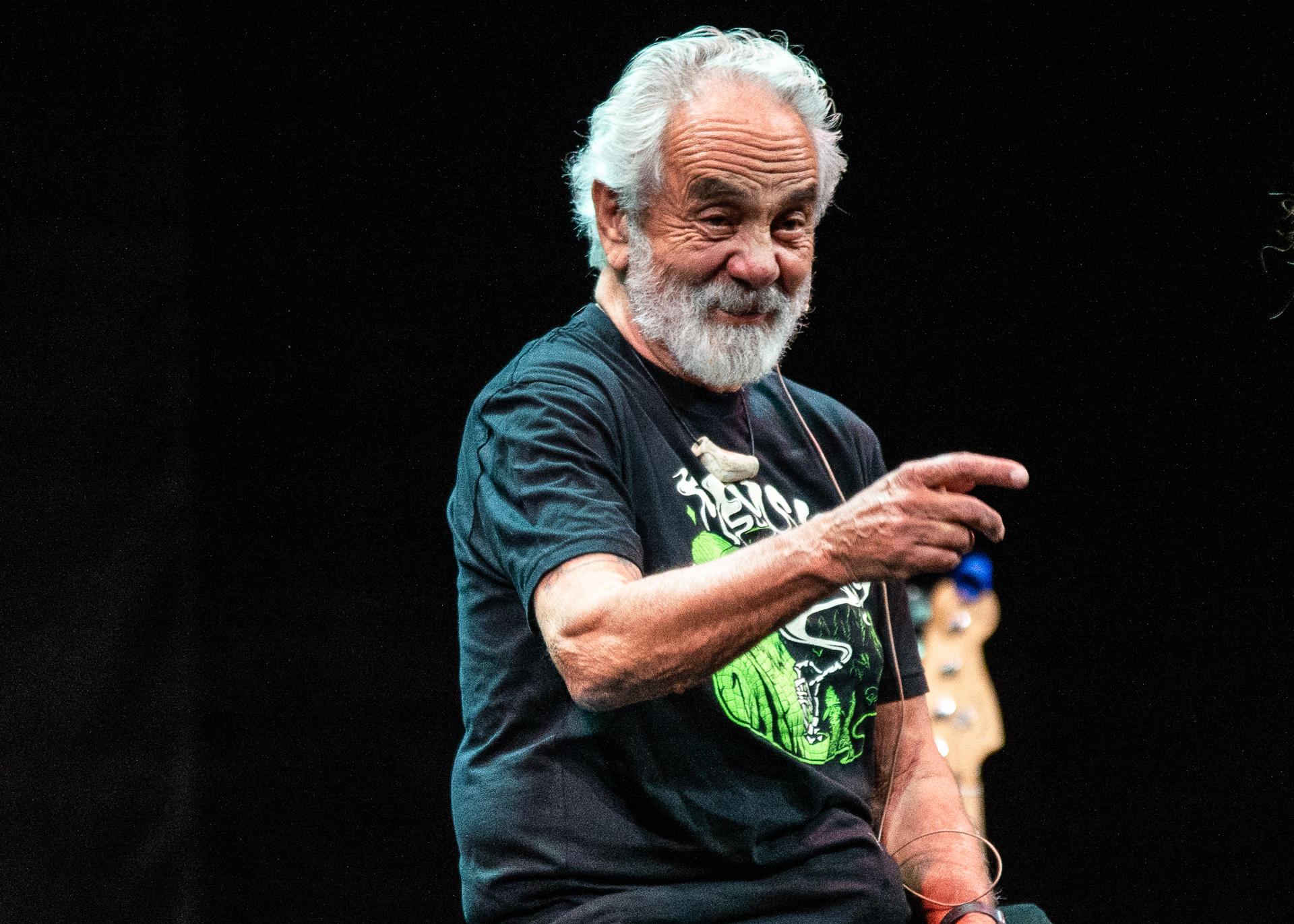 Tommy Chong sits on a stool, his face lit up with laughter as he playfully points towards the audience, creating a moment of shared joy and connection.