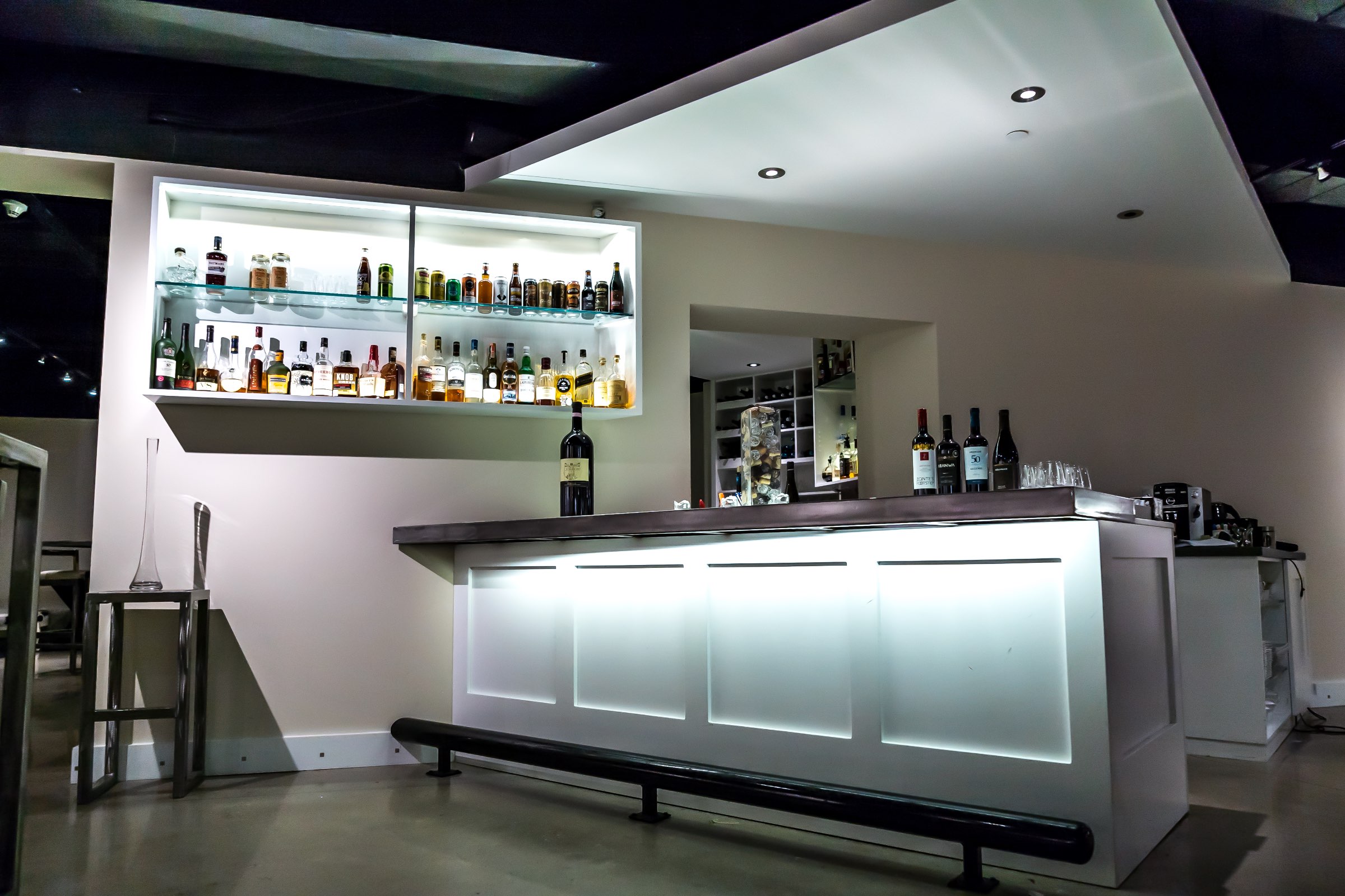 The lounge bar is shown at an angle and spotlit using dramatic lighting, with all the drinks available in a wall mounted display case to the left.